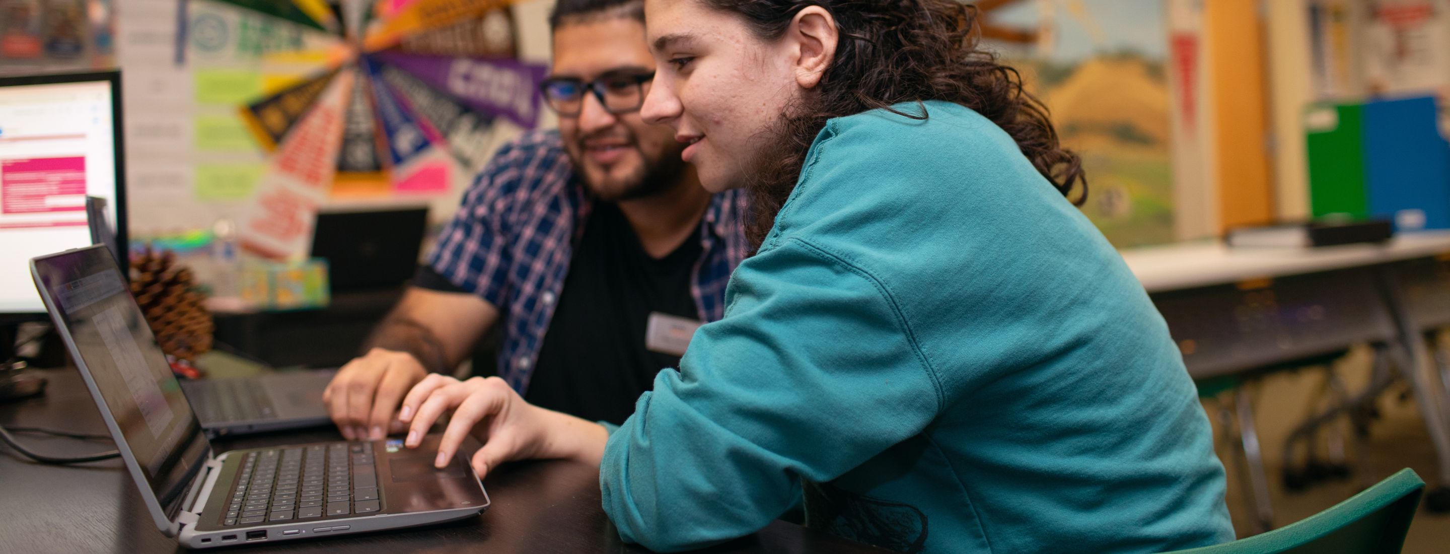 A student and teacher sitting at a desk and looking at a laptop together.