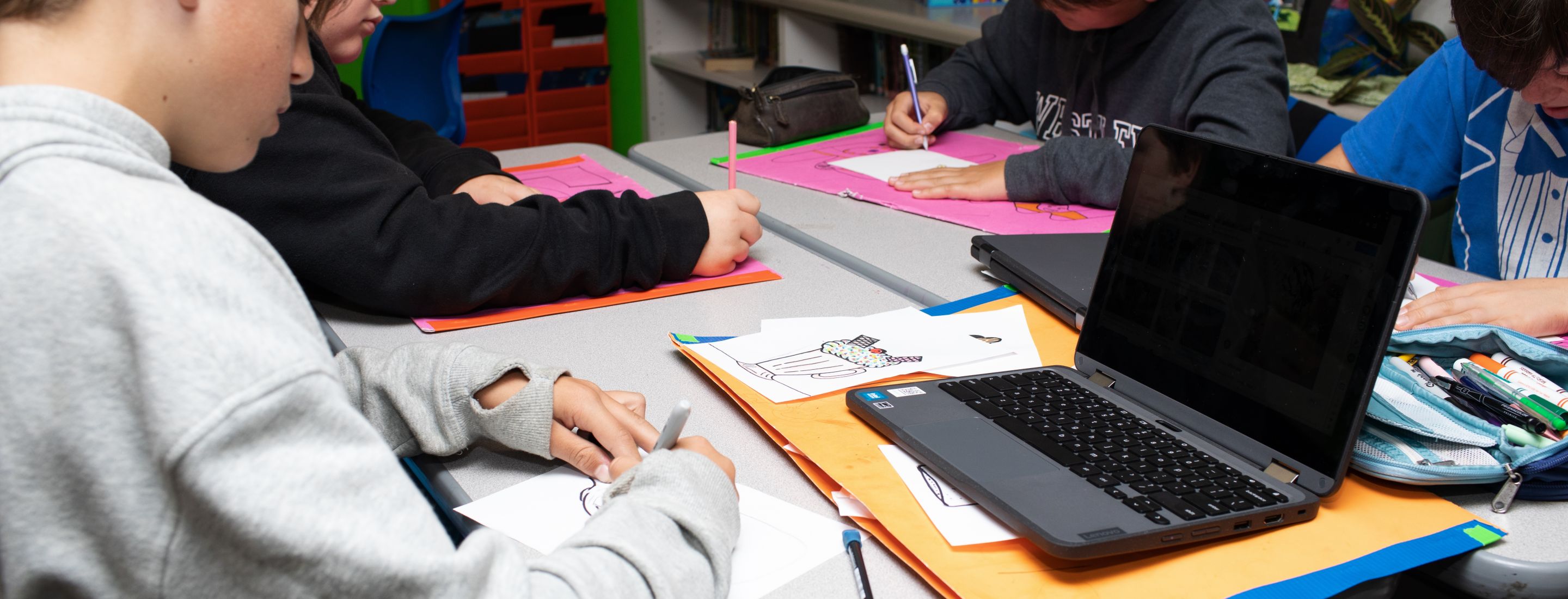 A student sitting at a desk, writing on a piece of paper, with a laptop open in front of them.